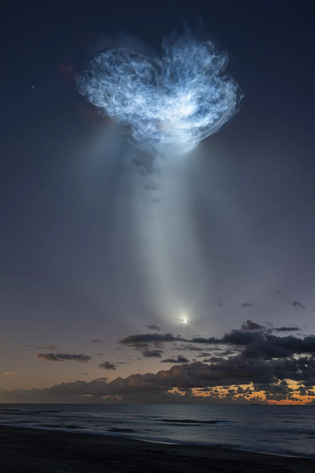 The exhaust plumes of a SpaceX Falcon 9 rocket carrying the company’s Dragon spacecraft are seen illuminated by sunlight against the predawn sky.