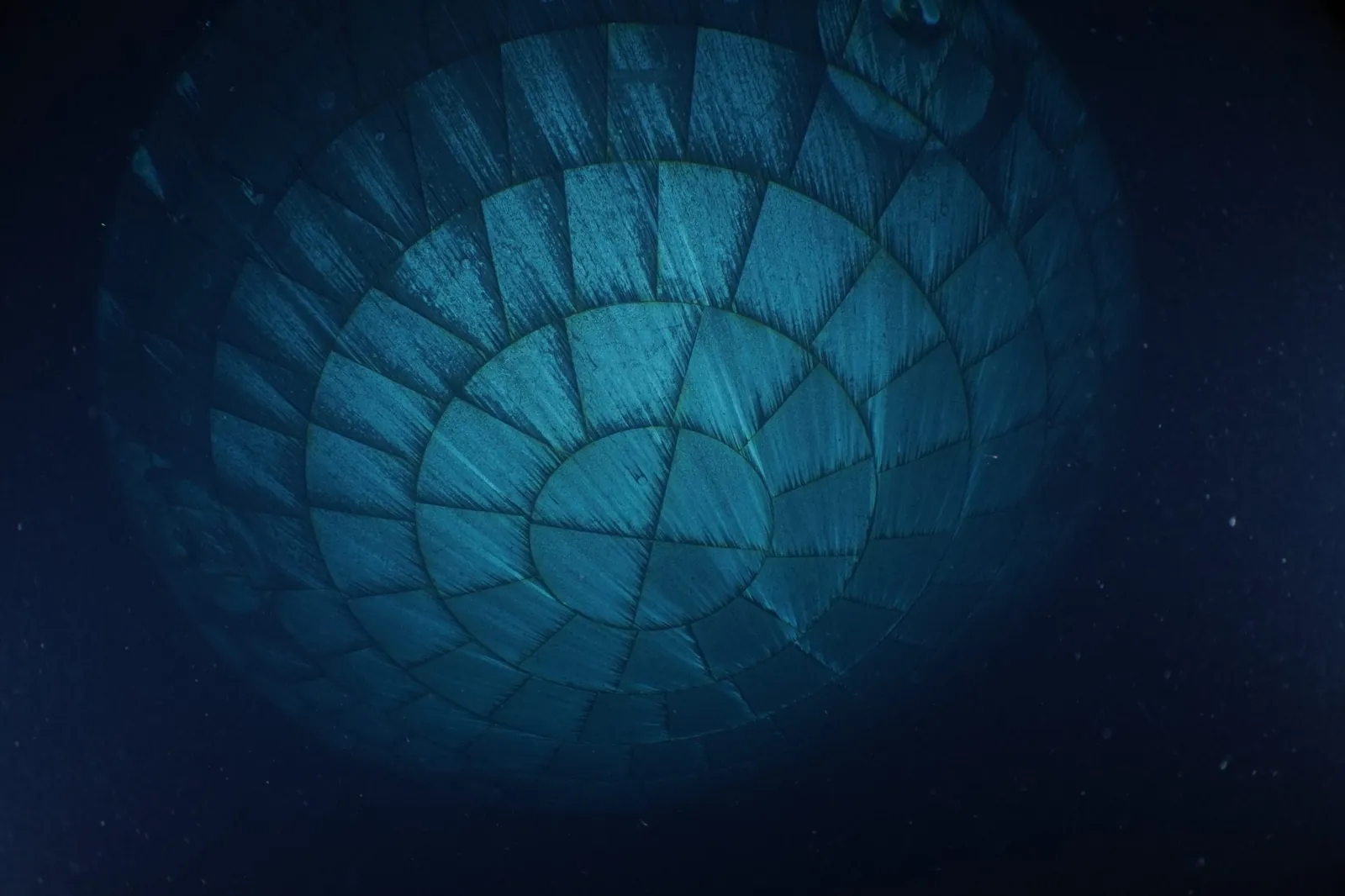 The Orion spacecraft's heat shield dominates this underwater photo. Due to the water, the heat shield appears to be teal-colored.