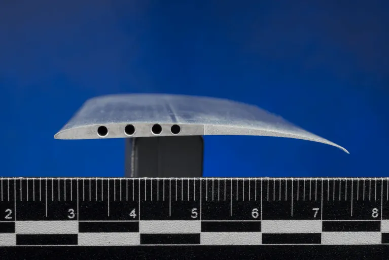 A close-up view of a cross-section of the Ingenuity rotor blade, also called an airfoil. The blade is shaped like an arched teardrop with holes drilled into the side.
