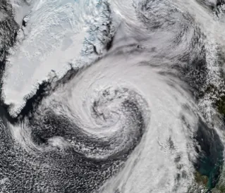 Storm clouds in an expanding spiral are centered near southern Iceland. The system extends across the North Atlantic from Greenland to the UK.