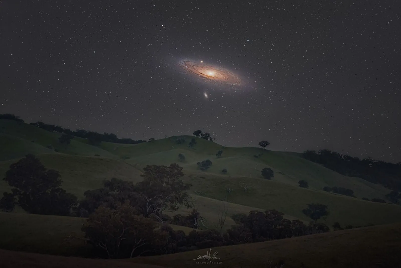 The Andromeda galaxy above rolling hills.