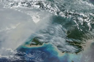 Smoke covers much of the southern third of New Guinea, while clouds and east-west-running mountain ranges are visible in the northern part of the island.