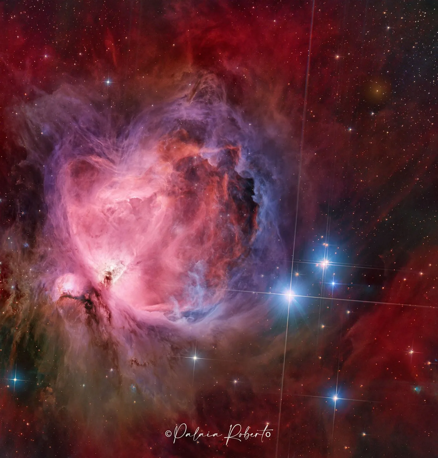 A starfield features a large and colorful nebula in its center, filled with dark dust and glowing gas in red and blue.