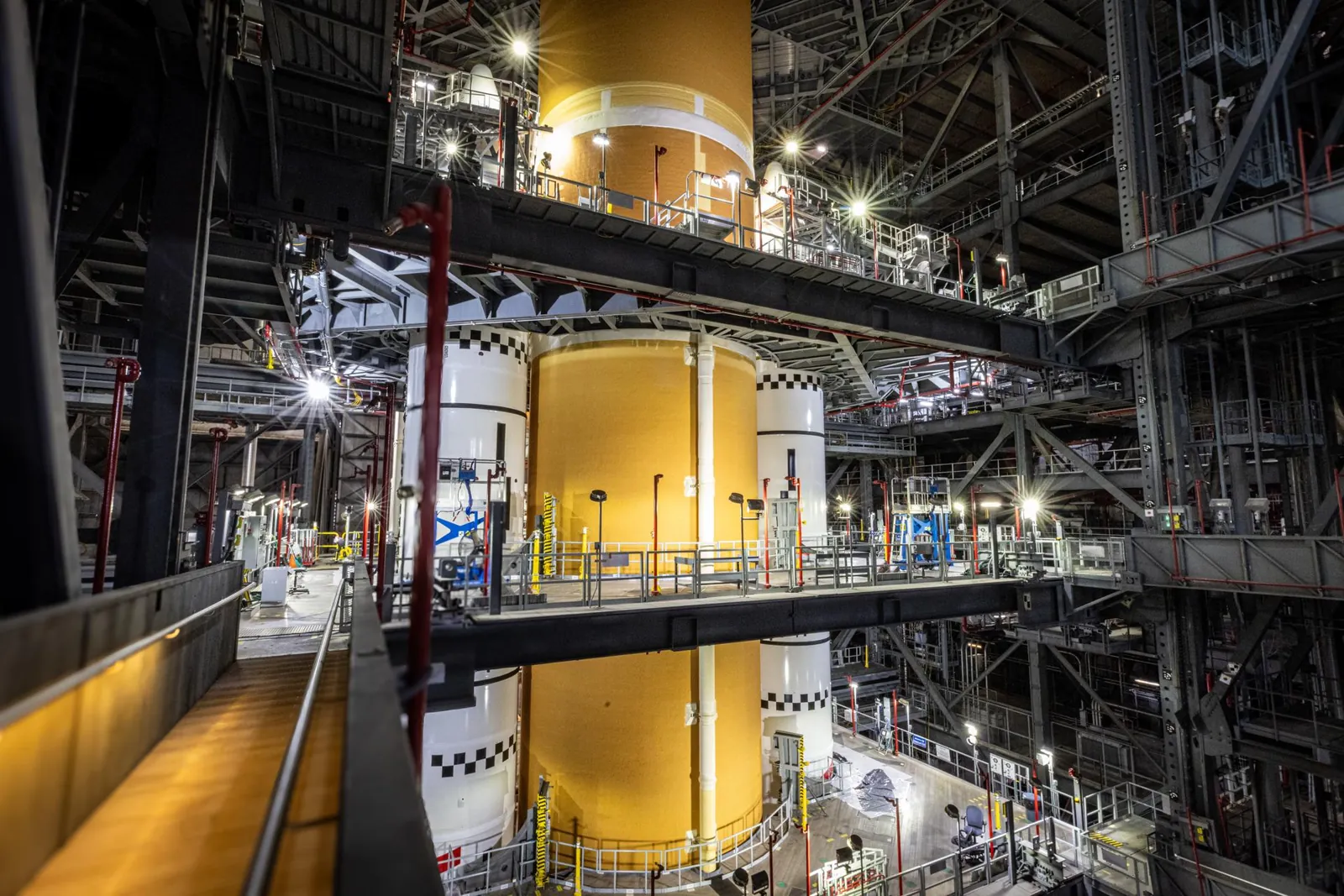 The central portion of the Space Launch System rocket stack is seen from a platform across the central aisle in the Vehicle Assembly Building. The nose cones of the solid rocket booster flank the oran